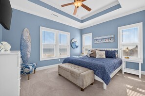Une chambre à coucher avec un lit, un ventilateur de plafond, une grande fenêtre et une œuvre d’art accrochée au mur.
