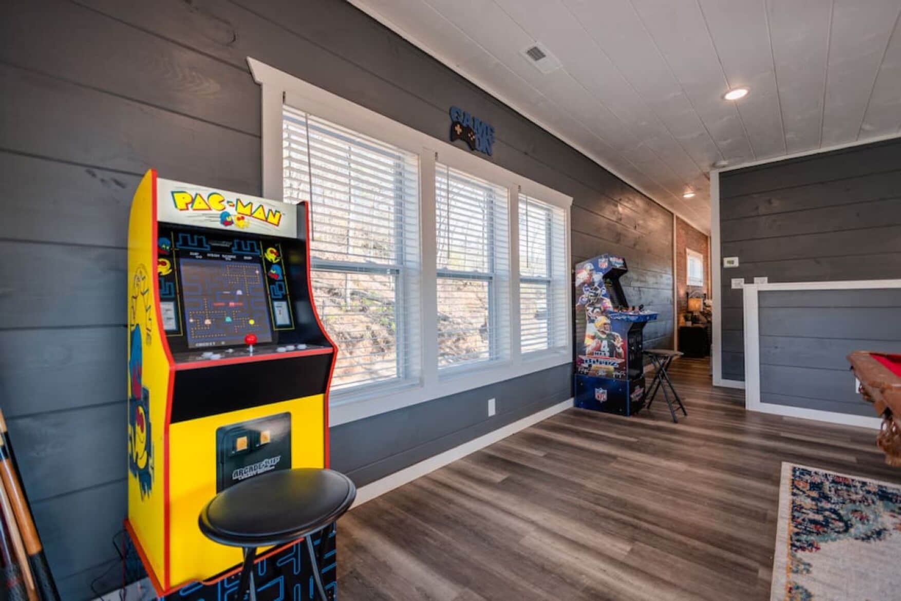 A room with a Pac-Man arcade machine, a small table, and a window with blinds.