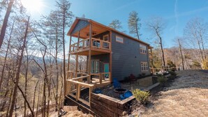 A two-story cabin with a balcony, surrounded by trees and a clear sky.