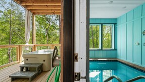A wooden deck with a hot tub, a small table, and a pool with a view of trees.