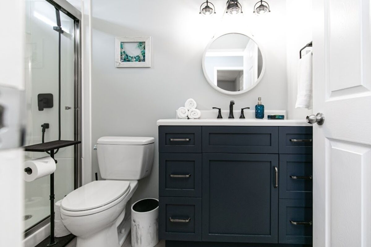 Un bagno moderno con il water bianco, mobili scuri, uno specchio rotondo e una cabina doccia in vetro.