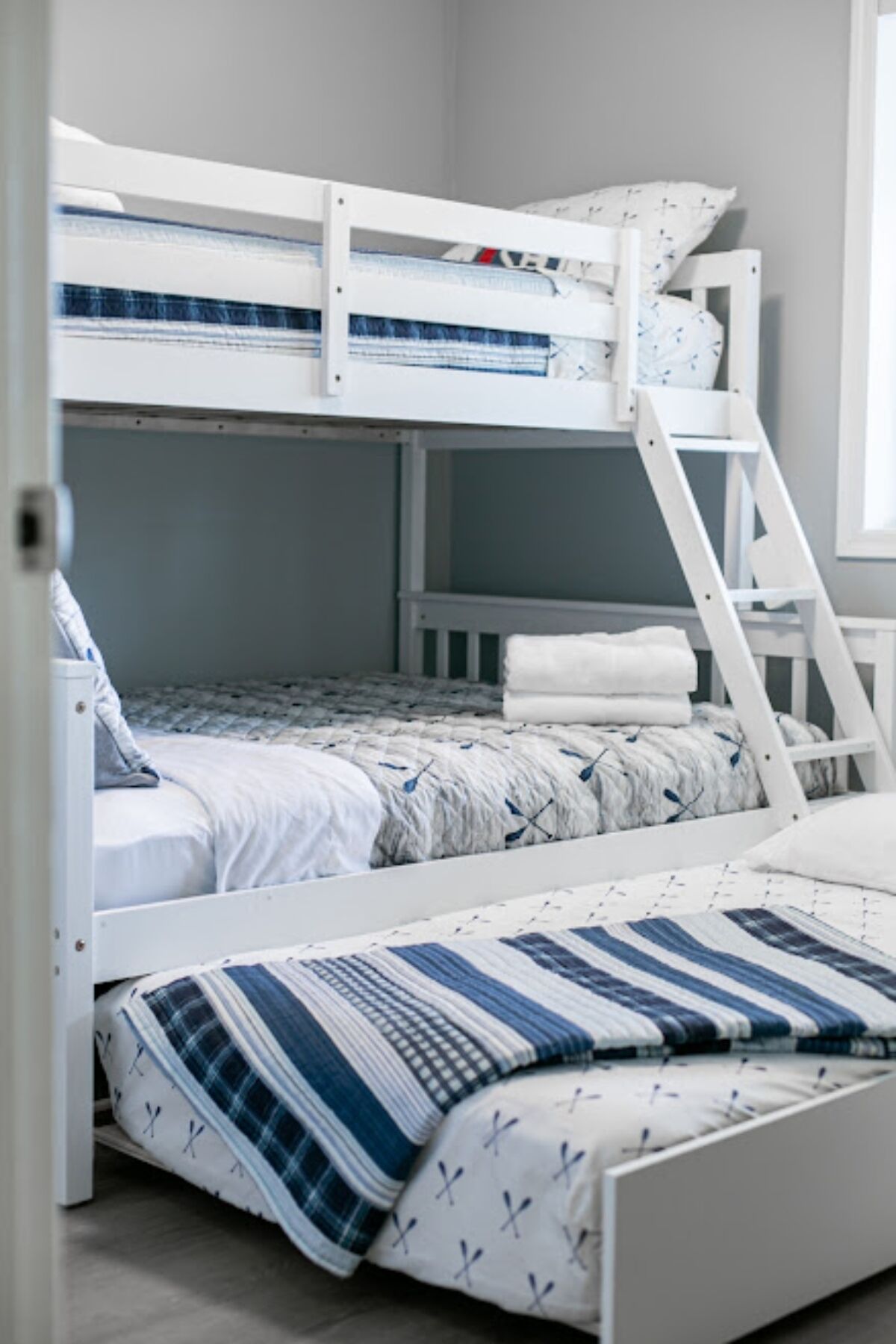 A bunk bed with a ladder, white bedding, and a plaid blanket.