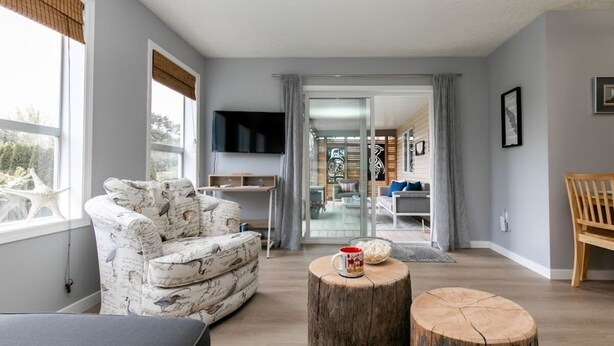 A modern living room with a patterned armchair, a coffee table, and a television mounted on the wall. - Lovely 2 bedroom suite steps from The beach (Victoria)