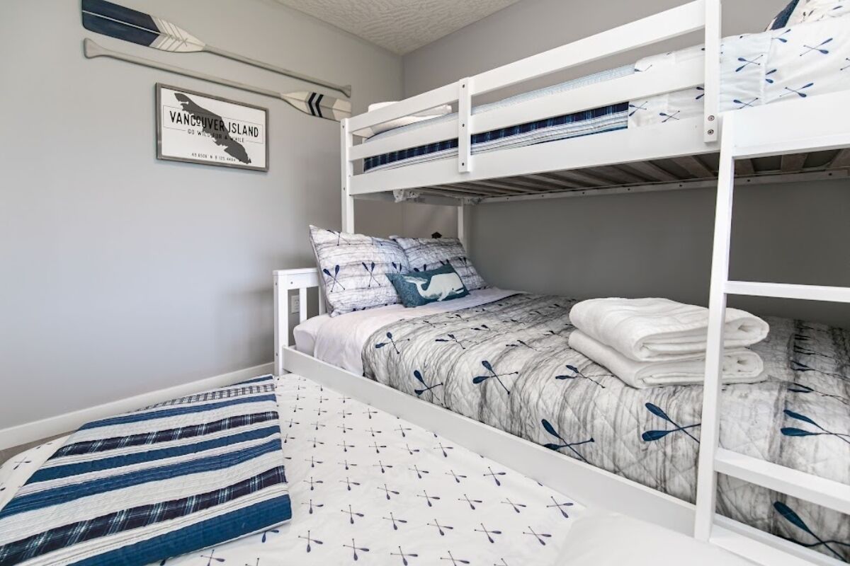 Een slaapkamer met stapelbedden, een kaart van Vancouver Island aan de muur, een gestreept vloerkleed en een bed met een bladprintendekbed.