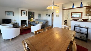 A living room with a wooden dining table, white sofas, a TV, and a fireplace.