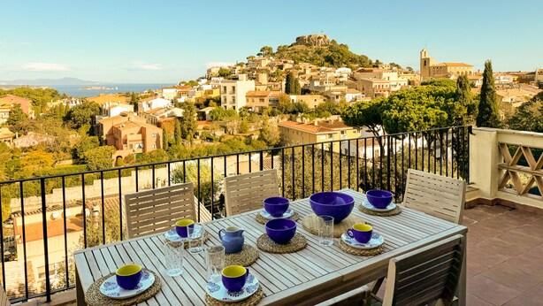A terrace with a table set for dining, overlooking a hillside town with historic buildings and a prominent church tower.