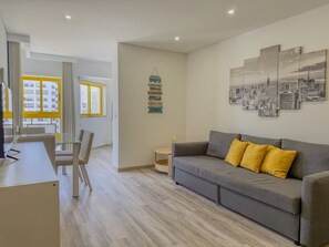 Una sala de estar moderna con un sofá gris, almohadas amarillas, una mesa de centro de cristal y una pintura con un paisaje urbano.