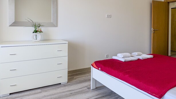 A bedroom with a white dresser, a red bedspread, and a mirror on the wall. - #150 Praia da Rocha by Home Holidays (Portimão)