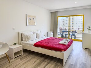 Una habitación de hotel moderna con cama, escritorio, silla y balcón con vistas a edificios.
