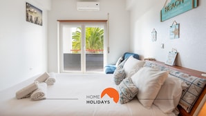 Quarto com cama, sofá e vista para palmeiras, com uma placa que diz 'BEACH'.