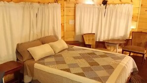 Une pièce chaleureuse, aménagée dans un chalet en bois, avec un grand lit, deux fauteuils, une petite table et une fenêtre avec des rideaux.