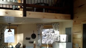 Une cuisine équipée d’une cuisinière, d’un évier et de placards. On y trouve des fenêtres avec des rideaux, un luminaire suspendu et un réfrigérateur.
