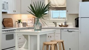 A modern kitchen with white cabinetry, a central island, wicker stools, and a potted plant. - Sandy Shores - Near Redfern (St. Simons Island)