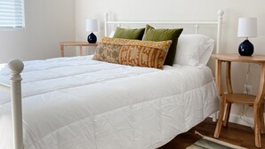 A neatly made bed with white bedding, two pillows, and a wooden headboard. There are two bedside tables with lamps, a window with blinds, and a patterned rug on the floor. - Near Downtown, Convenient to Restaurants, 2 Cruiser Bikes To Explore With! (Prescott)