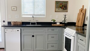 A kitchen with a dishwasher, stove, and sink. There is a window with blinds, a painting on the wall, and a wooden cutting board. - Near Downtown, Convenient to Restaurants, 2 Cruiser Bikes To Explore With! (Prescott)
