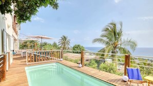 A wooden deck with a pool, outdoor furniture, and a view of the ocean.