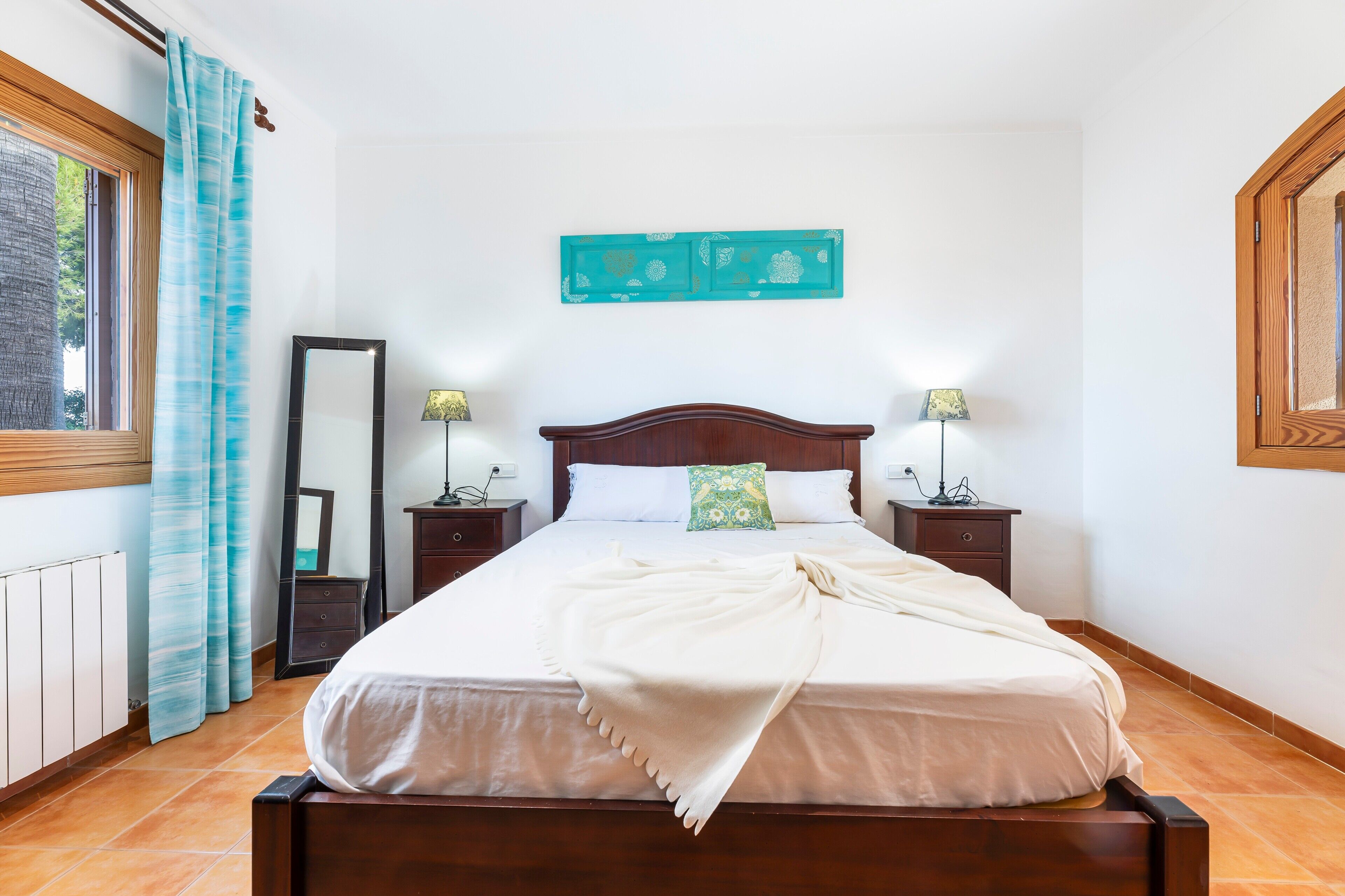 A neatly made bed with a white blanket, a wooden headboard, and two bedside lamps.