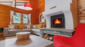 A cozy living room with a fireplace, a sofa, a red chair, and a round wooden coffee table. - Chalet Soleada with Fireplace and Terrace for 5, Pian San Giacomo, Mesocco, Switzerland (Pian San Giacomo, Mesocco)