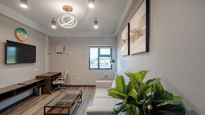 A modern living room with a flat-screen TV, wooden shelving, a sofa, a coffee table, and a large plant. - Kekehyu Business Hotel (Valencia)