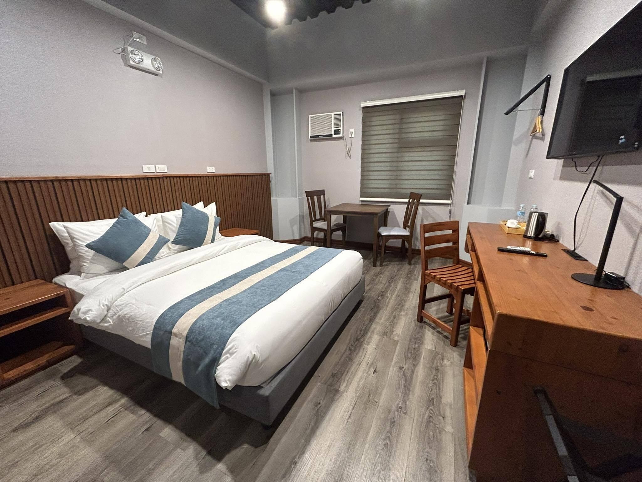 A hotel room with a bed, a desk, a chair, a TV, and a window with blinds.
