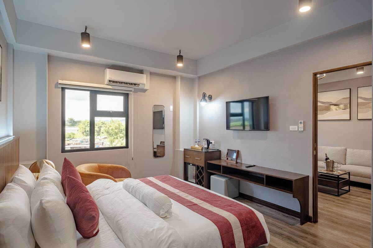 Moderni hotellihuone, jossa on suuri sänky, työpöytä, televisio ja ikkuna, josta avautuu näkymä vehreään maisemaan.