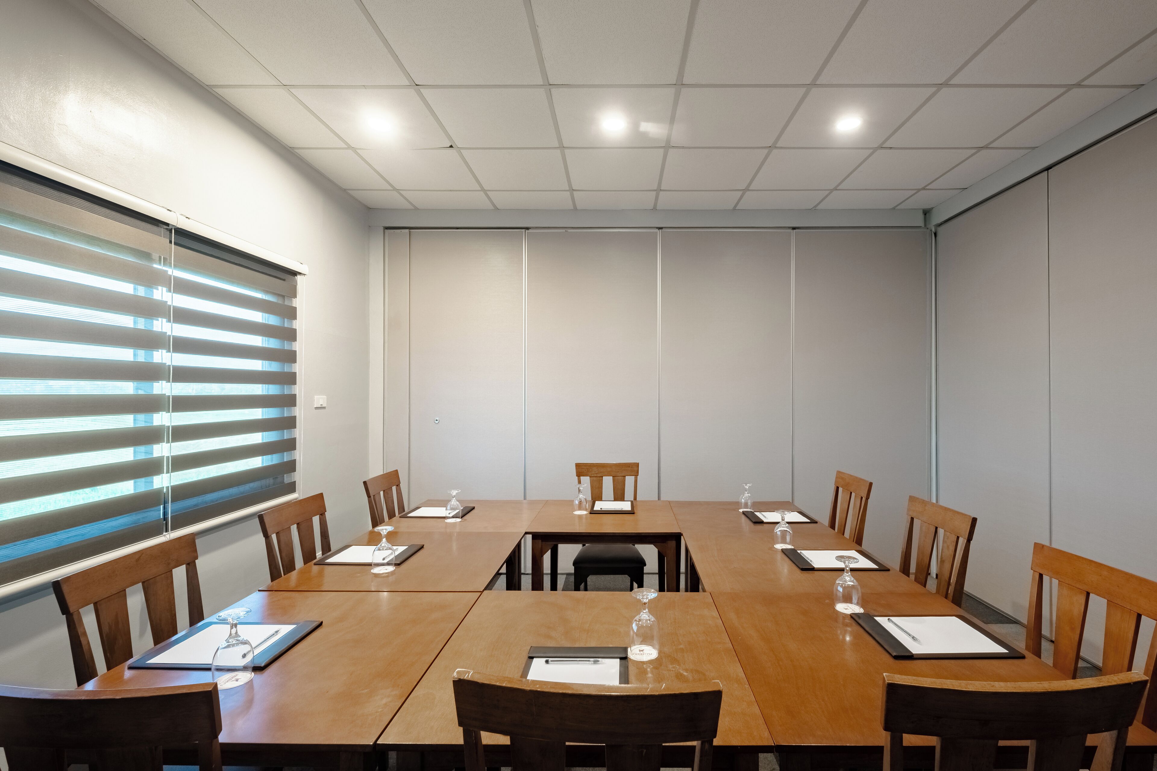 A conference room with a long table, wooden chairs, and a window with blinds.