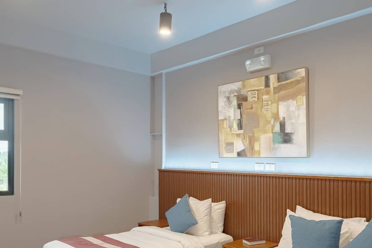 Hotellihuone, jossa on kaksi sänkyä, puinen pääty, moderni abstrakti maalaus ja upotetut kattovalaisimet.