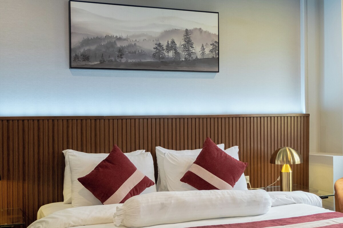 A neatly made bed with white and red bedding, a wooden headboard, and a framed picture on the wall above.
