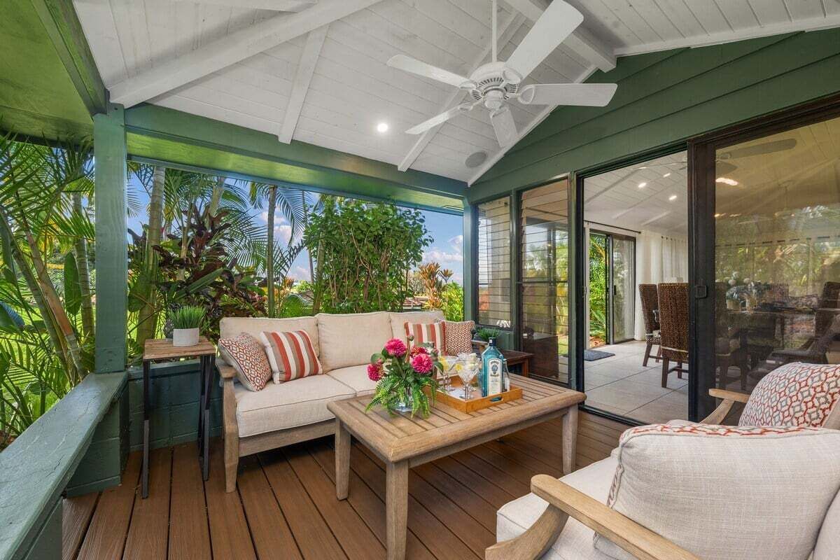 A covered outdoor seating area with a wooden table, a sofa, and a ceiling fan.