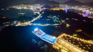 Un hotel moderno con piscina en la azotea, una zona costera bien iluminada y vistas a la ciudad.