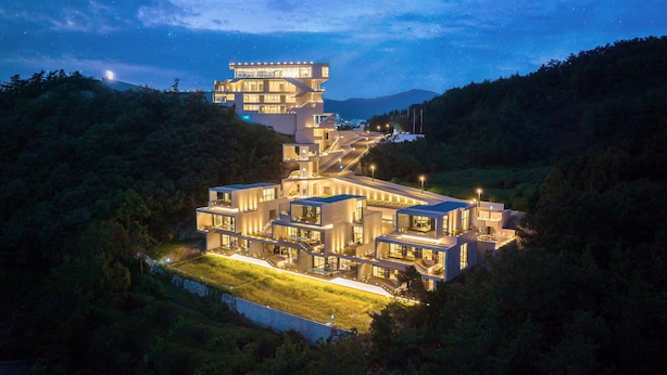 Un edificio moderno de varios pisos con un diseño arquitectónico único, rodeado de abundante vegetación y con un cielo estrellado de fondo.