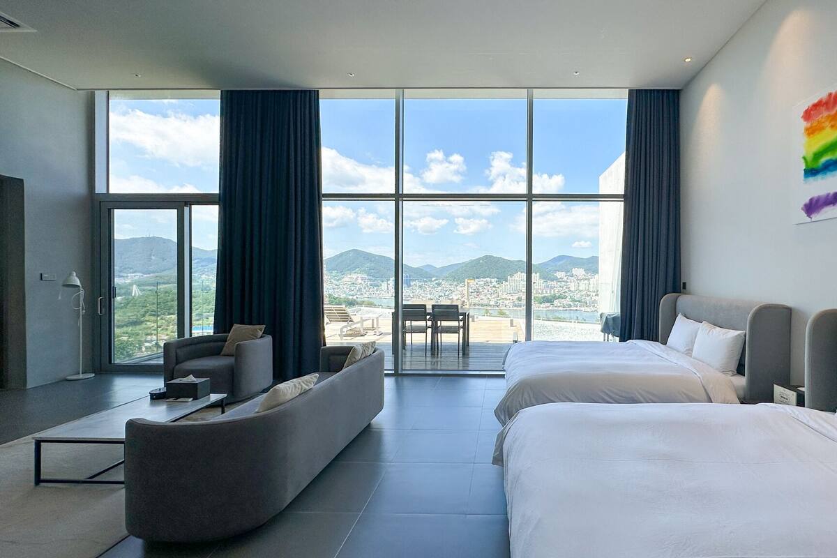 Habitación de hotel moderna con dos camas, un sofá y un amplio ventanal con vistas a la ciudad.