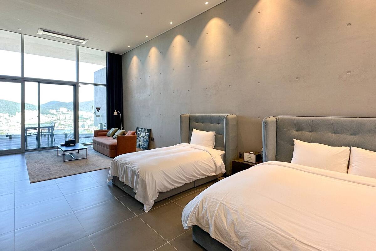 Una habitación de hotel moderna con dos camas, un sofá, una mesita y un ventanal con vistas a la ciudad.