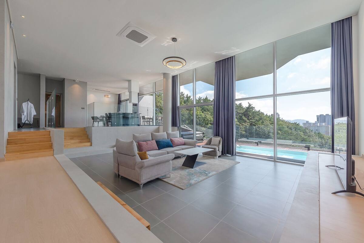 Un salón amplio con un sofá moderno, una mesa de centro y vistas a una piscina a través de grandes ventanales.