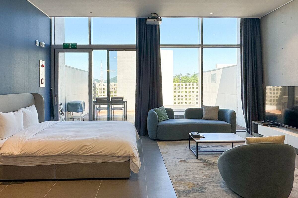 Una habitación de hotel moderna con una cama grande, un sofá, un televisor y un balcón con vista a la ciudad.