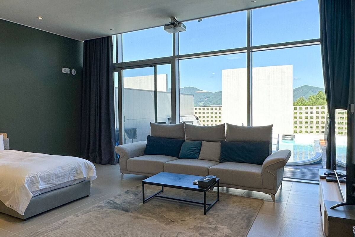 Una habitación de hotel moderna con una cama, un sofá, una mesita de centro y grandes ventanales con vistas a la ciudad.