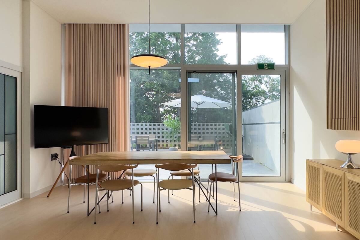 Una sala moderna con un ventanal grande, un televisor de pantalla plana, una mesa de comedor con sillas y un aparador de madera con una lámpara.