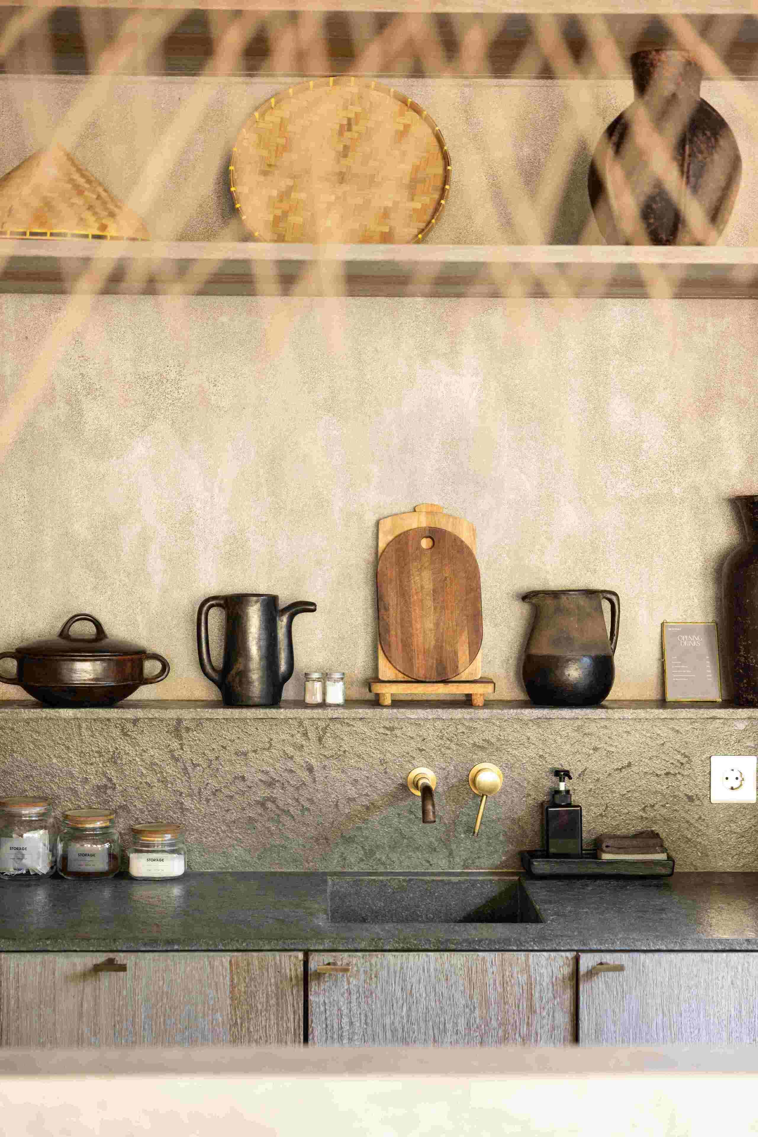 A kitchen with a stone countertop, wooden cabinets, and various kitchenware including a pot, jug, and wooden board.