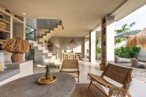 Un intérieur moderne avec une table ronde en pierre, des chaises en osier et un escalier menant à un niveau supérieur.