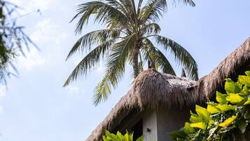A building with a thatched roof, a palm tree, and lush greenery.