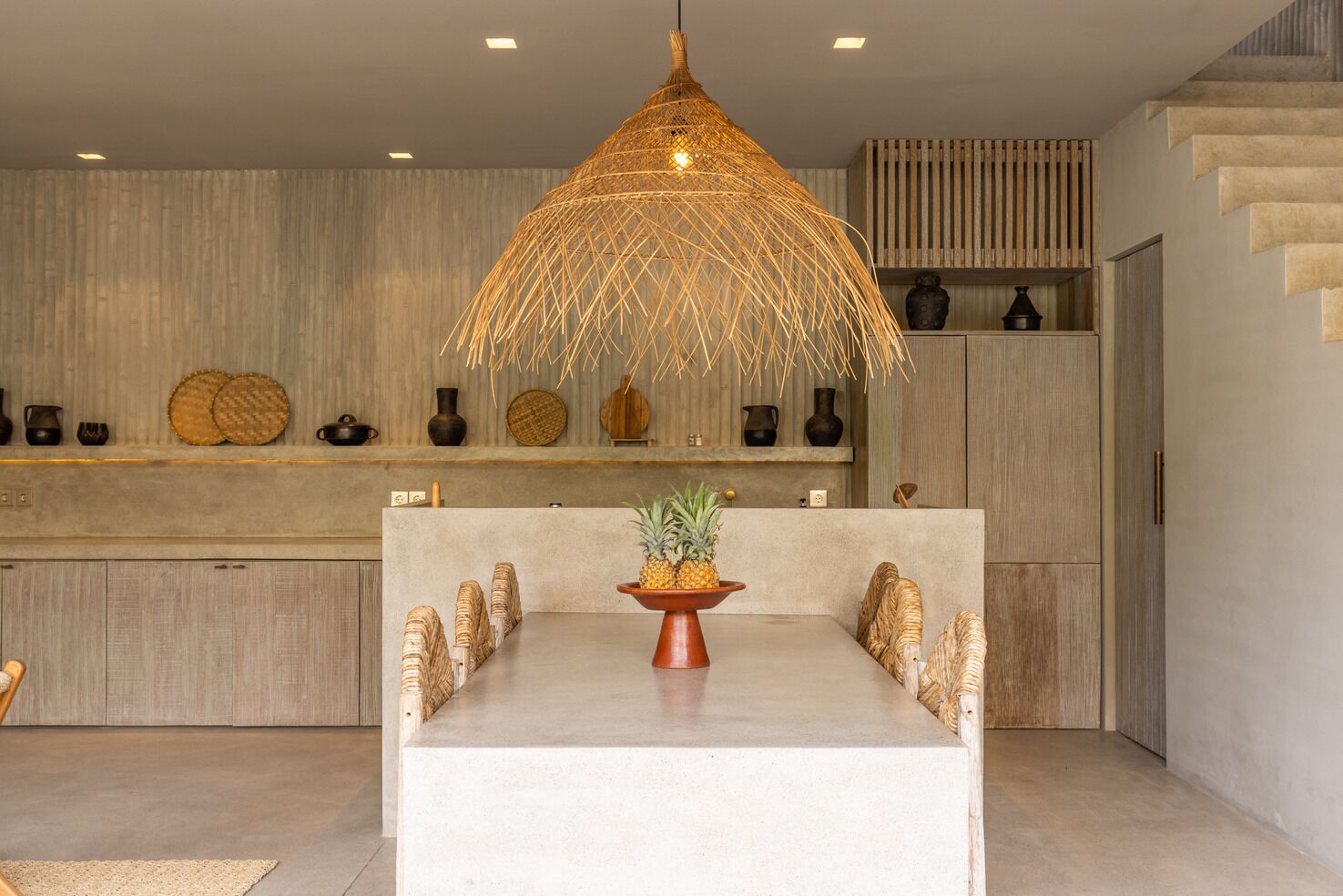 A modern kitchen with a central island, a hanging light fixture, and a variety of decorative items on the shelves.