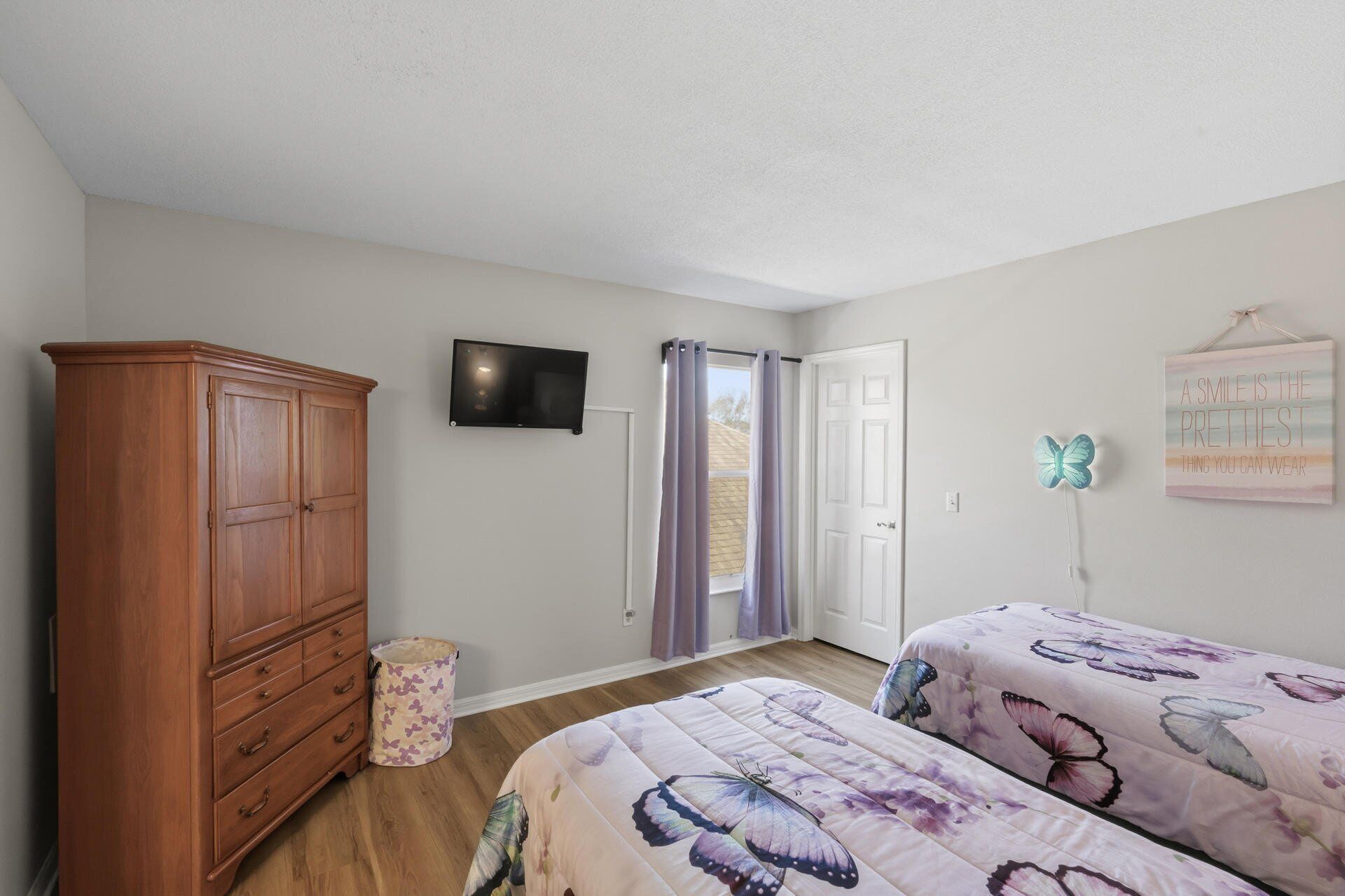 A bedroom with two beds, a wooden wardrobe, a television, and a butterfly wall decoration.