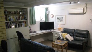 Un espace de vie compact comprenant un bureau, deux fauteuils en cuir, une bibliothèque, un téléviseur et une fenêtre avec des rideaux.