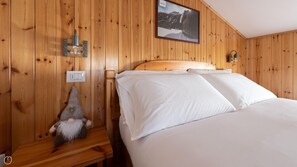 Et rum med træpaneler, en seng, en vægmonteret lampe, et billede og en lille pynteting.