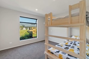 A bunk bed room with a large window offering a view of a house and garden.