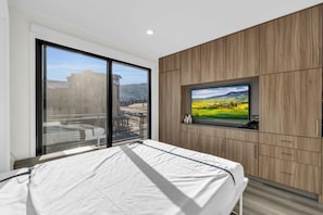 A bedroom with a large window, a bed, a television, and wooden paneling.
