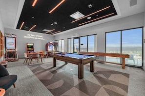 A pool table in a room with large windows, arcade games, and a message on the wall.
