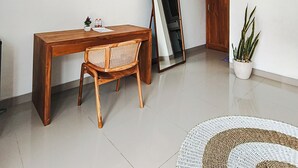 Un salon minimaliste avec une table à manger en bois, une chaise en osier, un grand miroir, une plante en pot et un tapis rond en fibres tressées.