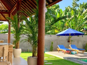 Relax by the pool under a shaded pergola with a table and chairs.