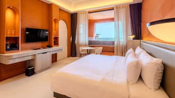 Habitación de hotel con una cama grande, un escritorio con televisor de pantalla plana, una mesita pequeña y vistas al mar a través de amplios ventanales.